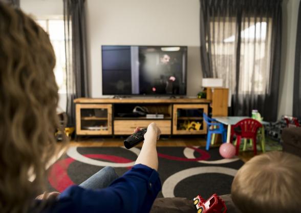 A mother and child sitting on a couch holding a remote up to the TV